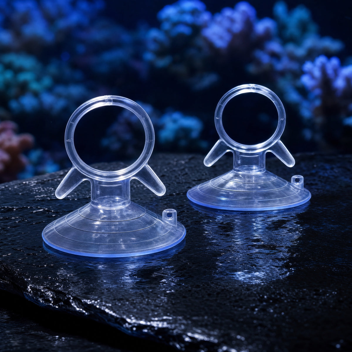Two clear Reefphyto aquarium suction cups with ring holders on wet slate in front of a reef tank