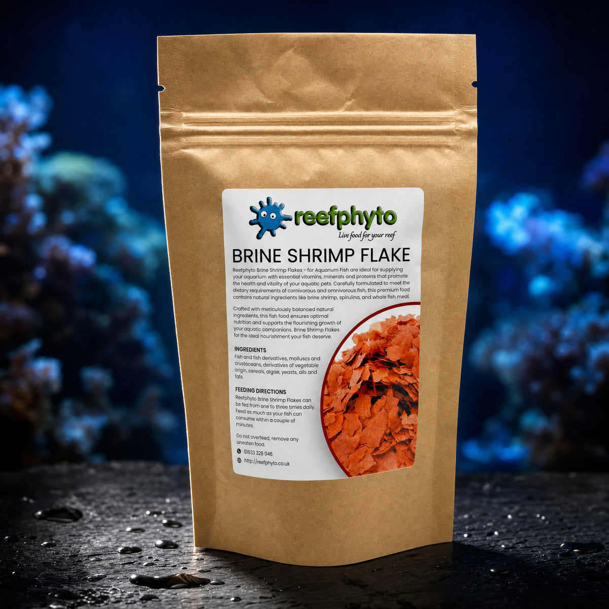 Reefphyto Brine Shrimp Flake kraft pouch on wet slate in front of a blue-lit reef aquarium