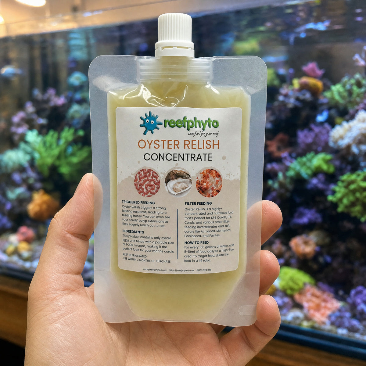 Reefphyto Oyster Relish Concentrate pouch held in a hand in front of a reef aquarium